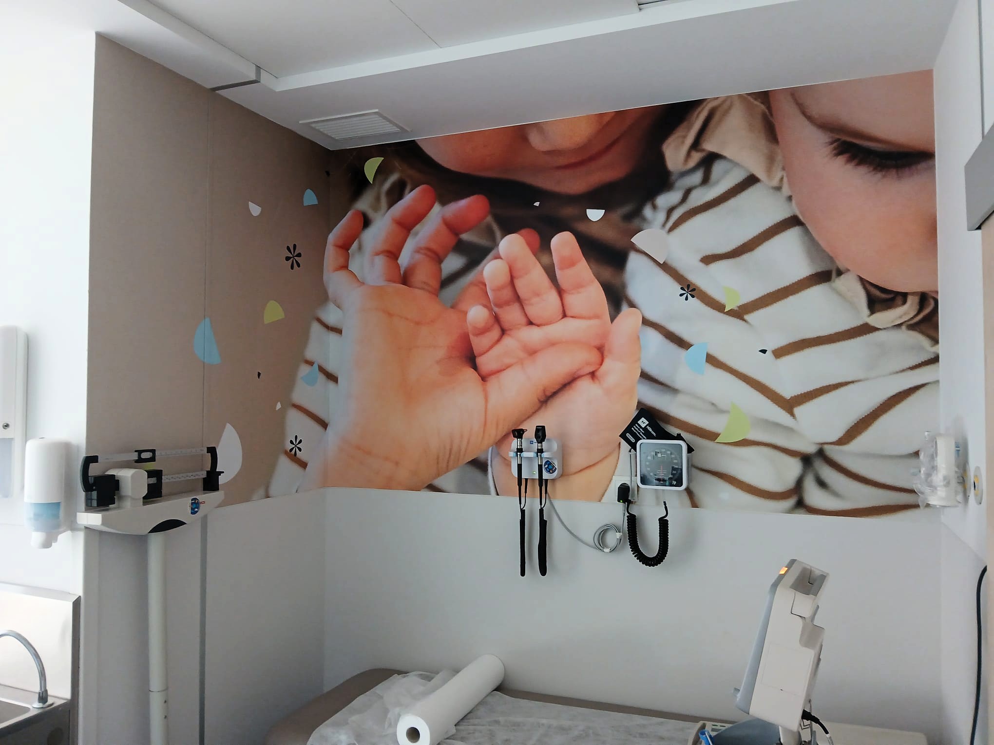 Vinilo de pared con una fotografía de un bebé y unas manos; delante se ven varios instrumentos sujetos a la pared.